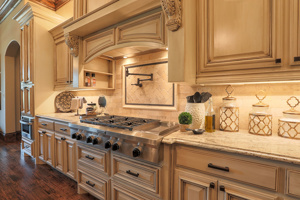 Inspiration for a large mediterranean l-shaped dark wood floor and brown floor eat-in kitchen remodel in Dallas with raised-panel cabinets, beige cabinets, granite countertops, beige backsplash, travertine backsplash, stainless steel appliances, an island and beige countertops