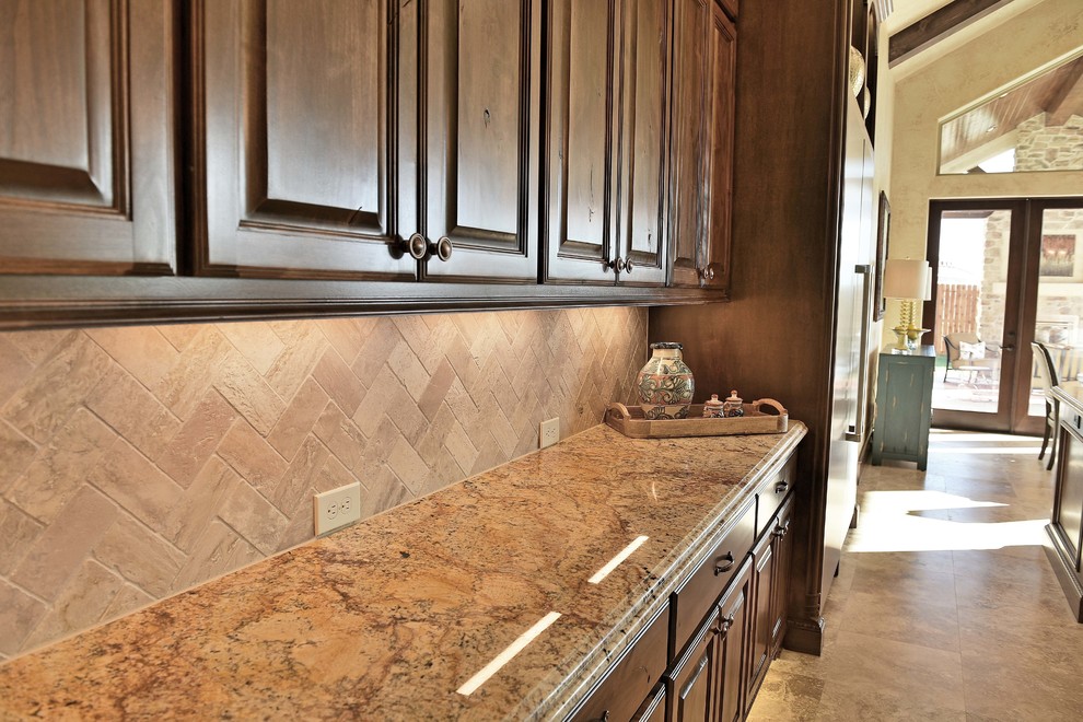 Inredning av ett medelhavsstil stort kök, med luckor med upphöjd panel, bruna skåp, granitbänkskiva, beige stänkskydd, stänkskydd i stenkakel, rostfria vitvaror, travertin golv, flera köksöar och beiget golv