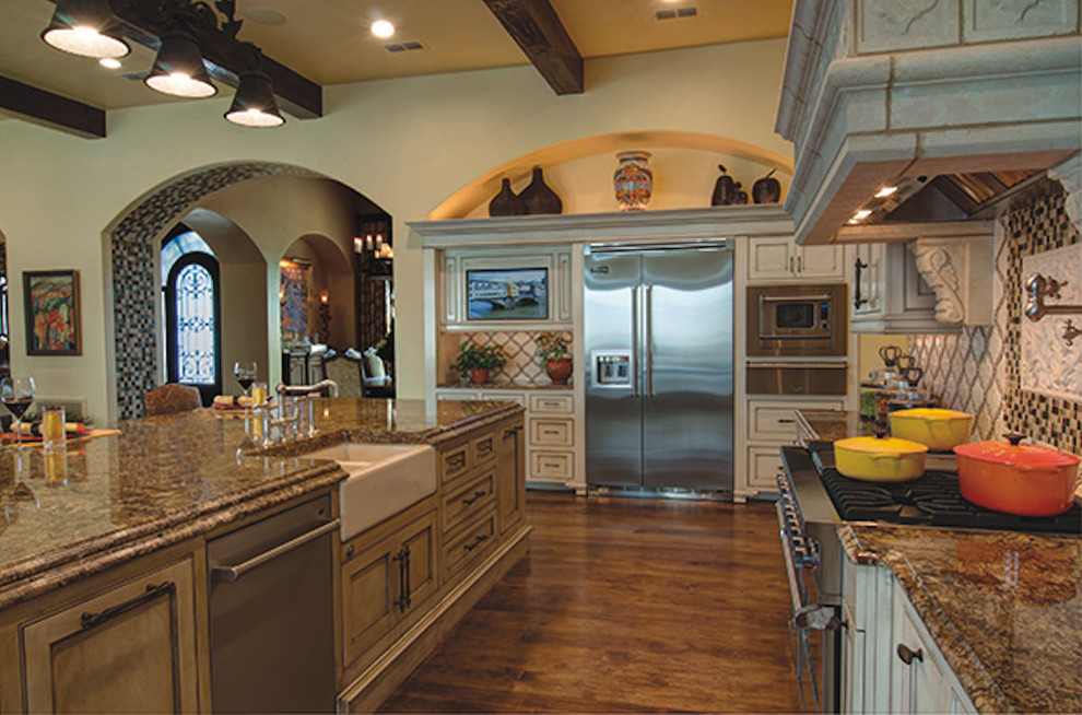 Inspiration for a large mediterranean medium tone wood floor open concept kitchen remodel in Dallas with a farmhouse sink, beaded inset cabinets, white cabinets, granite countertops, white backsplash, glass tile backsplash, stainless steel appliances and an island