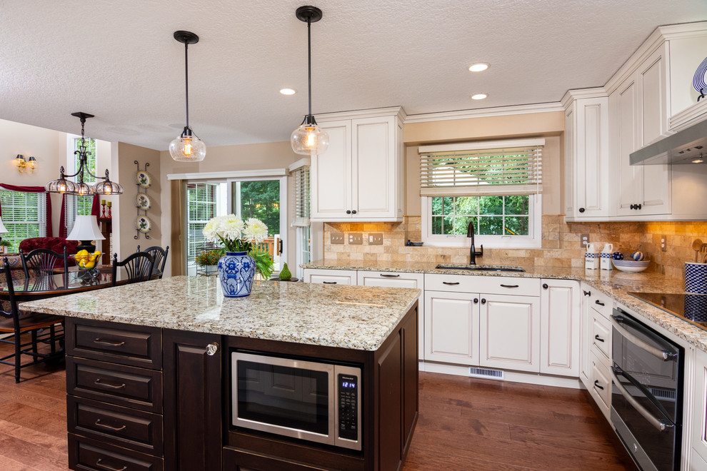Exempel på ett mellanstort klassiskt flerfärgad flerfärgat u-kök, med en undermonterad diskho, luckor med upphöjd panel, vita skåp, beige stänkskydd, rostfria vitvaror, mellanmörkt trägolv, en köksö, granitbänkskiva, stänkskydd i travertin och brunt golv
