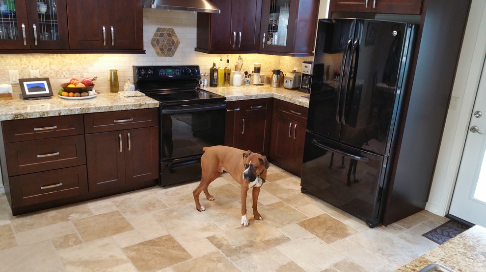 Idée de décoration pour une grande cuisine américaine chalet en U et bois foncé avec un évier posé, un placard à porte plane, un plan de travail en granite, une crédence beige, une crédence en carrelage de pierre, un électroménager noir, un sol en travertin et îlot.