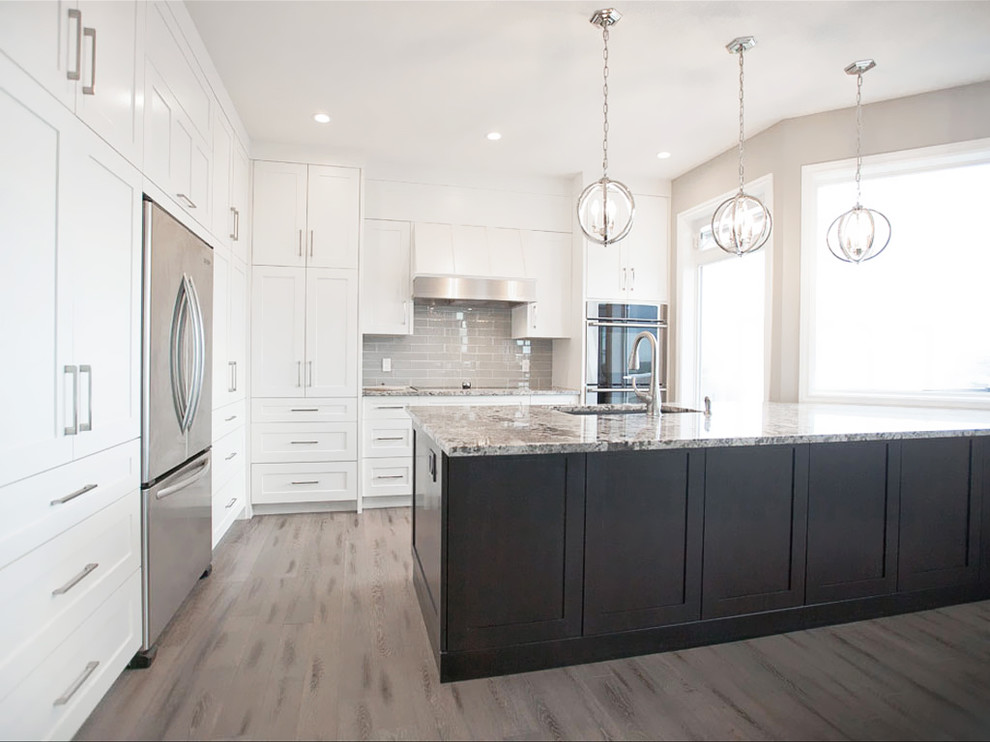 This is an example of a large classic l-shaped kitchen in Calgary with a submerged sink, shaker cabinets, white cabinets, granite worktops, grey splashback, metro tiled splashback, stainless steel appliances, medium hardwood flooring and an island.