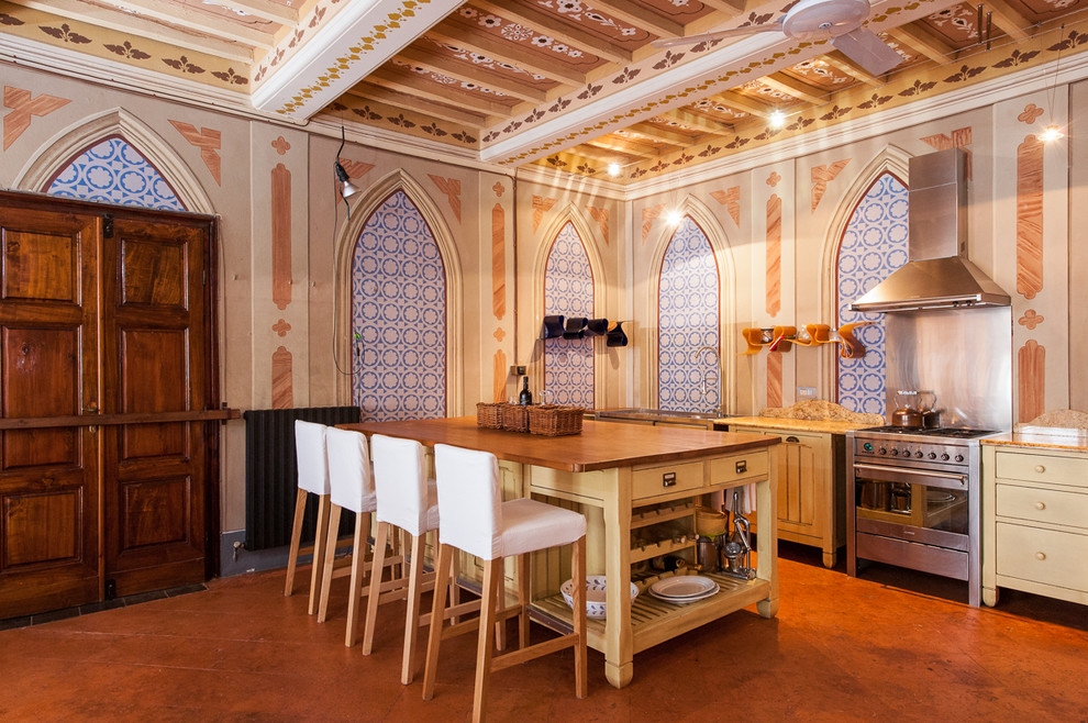Foto di una cucina mediterranea con ante lisce, ante gialle, top in legno, elettrodomestici in acciaio inossidabile e pavimento arancione