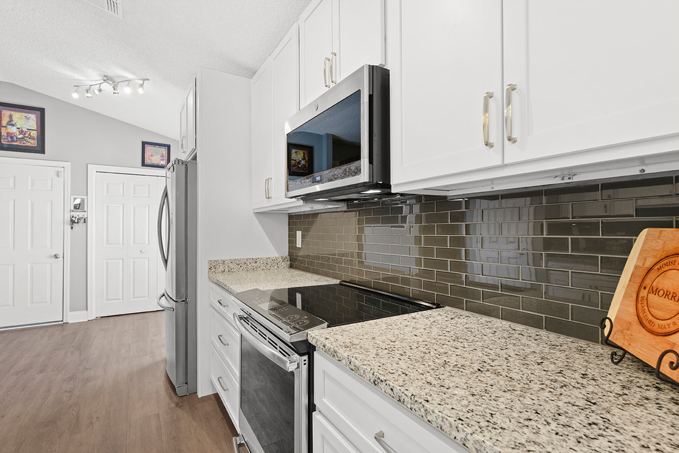 Bild på ett mellanstort funkis grå grått kök, med en enkel diskho, skåp i shakerstil, vita skåp, granitbänkskiva, grått stänkskydd, stänkskydd i glaskakel, rostfria vitvaror, vinylgolv och grått golv