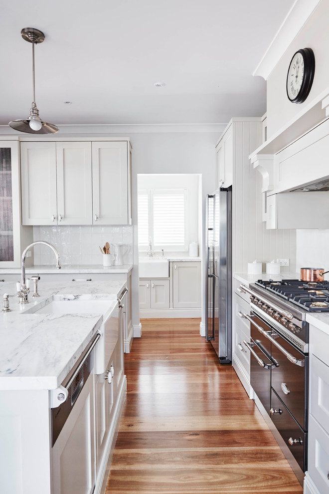Mittelgroße, Zweizeilige Klassische Wohnküche mit Landhausspüle, Schrankfronten im Shaker-Stil, grauen Schränken, Küchenrückwand in Weiß, Küchengeräten aus Edelstahl, braunem Holzboden und Kücheninsel in Sydney