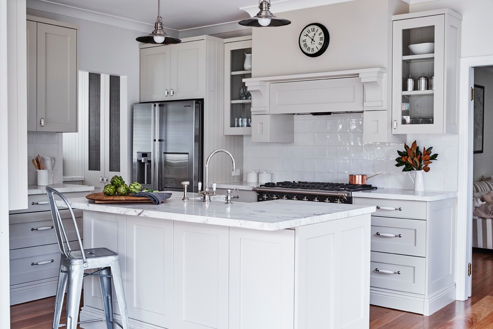 Mittelgroße Klassische Wohnküche in L-Form mit Landhausspüle, Schrankfronten im Shaker-Stil, grauen Schränken, Küchenrückwand in Weiß, Küchengeräten aus Edelstahl, braunem Holzboden und Kücheninsel in Sydney