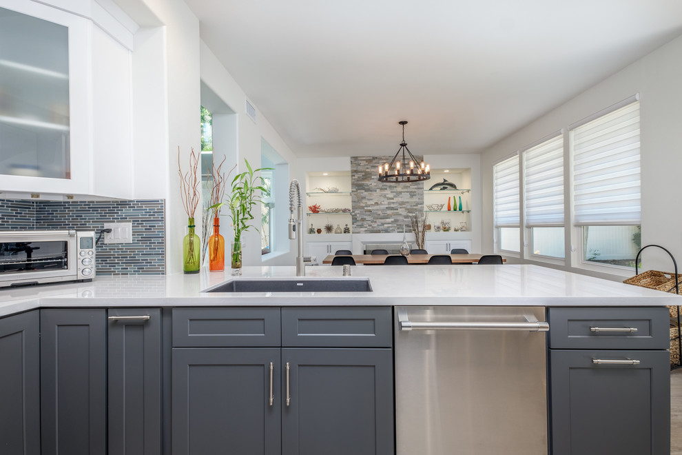 Mid-sized transitional u-shaped light wood floor and beige floor eat-in kitchen photo in Orange County with an undermount sink, shaker cabinets, white cabinets, solid surface countertops, multicolored backsplash, matchstick tile backsplash, stainless steel appliances and a peninsula