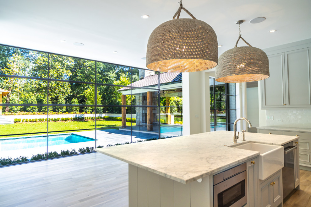 Large modern l-shaped open plan kitchen in Atlanta with a belfast sink, recessed-panel cabinets, grey cabinets, marble worktops, white splashback, ceramic splashback, stainless steel appliances, light hardwood flooring, an island, white floors, grey worktops and a timber clad ceiling.