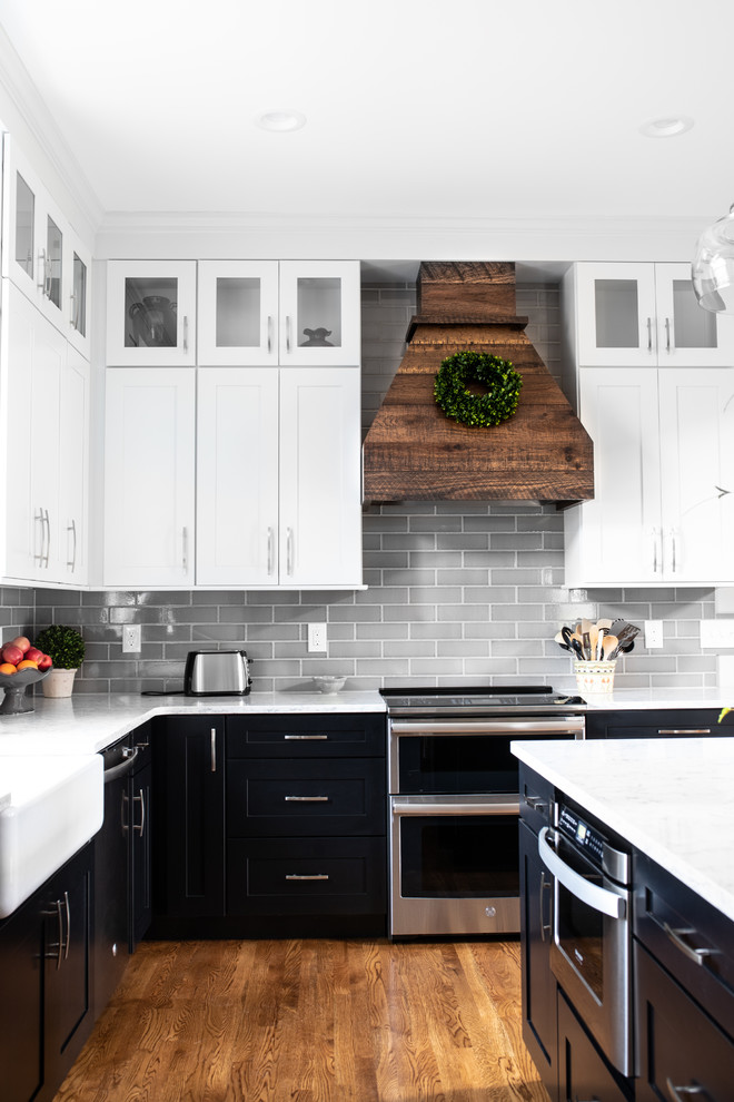 Bild på ett mellanstort lantligt vit vitt kök, med en rustik diskho, skåp i shakerstil, svarta skåp, bänkskiva i kvarts, grått stänkskydd, stänkskydd i tunnelbanekakel, rostfria vitvaror, mellanmörkt trägolv, en köksö och brunt golv