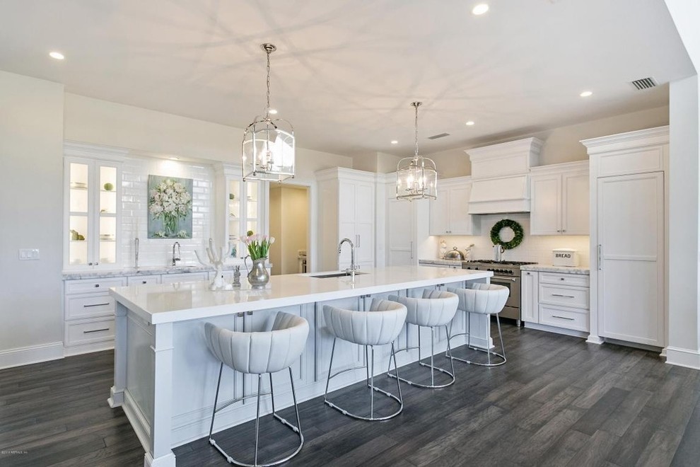 Inspiration for a traditional kitchen in Jacksonville with a submerged sink, glass-front cabinets, white cabinets, white splashback, metro tiled splashback, stainless steel appliances, dark hardwood flooring and an island.
