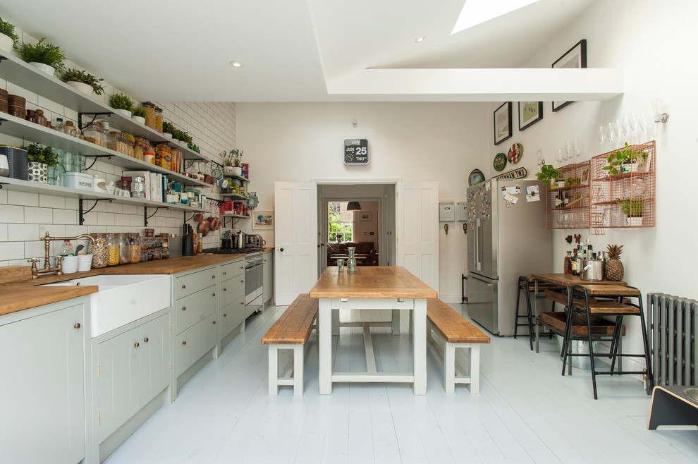 Inspiration for a farmhouse kitchen in London with a belfast sink, grey cabinets, white splashback, metro tiled splashback, stainless steel appliances, painted wood flooring and no island.