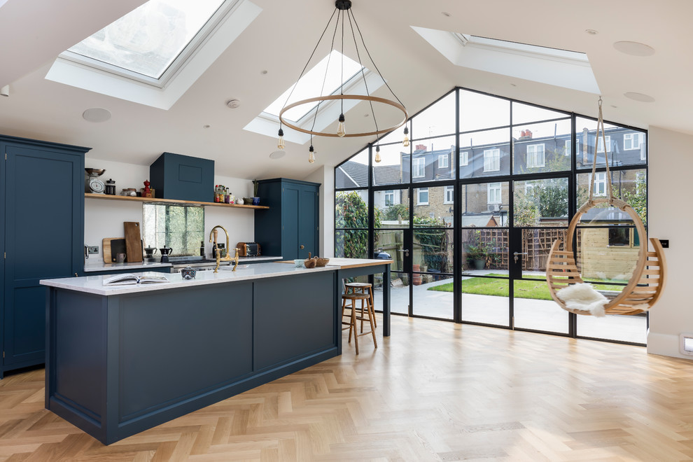 Photo of a medium sized contemporary single-wall open plan kitchen in London with a single-bowl sink, flat-panel cabinets, blue cabinets, marble worktops, an island, brown floors, grey worktops, mirror splashback, stainless steel appliances and light hardwood flooring.