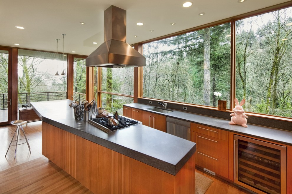 Moderne Küche mit Unterbauwaschbecken, flächenbündigen Schrankfronten, hellbraunen Holzschränken, Rückwand-Fenster, Küchengeräten aus Edelstahl, braunem Holzboden und Kücheninsel in Portland