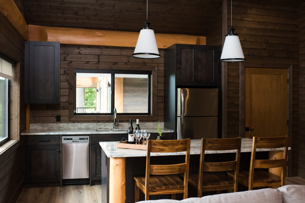 Design ideas for a rustic l-shaped open plan kitchen in Vancouver with a submerged sink, recessed-panel cabinets, dark wood cabinets, stainless steel appliances, medium hardwood flooring, an island, brown floors, grey worktops, granite worktops and window splashback.