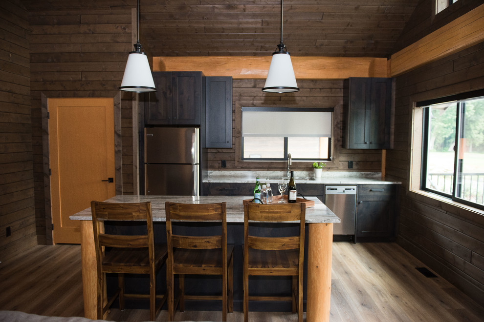Exempel på ett mellanstort rustikt grå linjärt grått kök med öppen planlösning, med en dubbel diskho, skåp i shakerstil, skåp i mörkt trä, granitbänkskiva, fönster som stänkskydd, rostfria vitvaror, laminatgolv, en köksö och brunt golv
