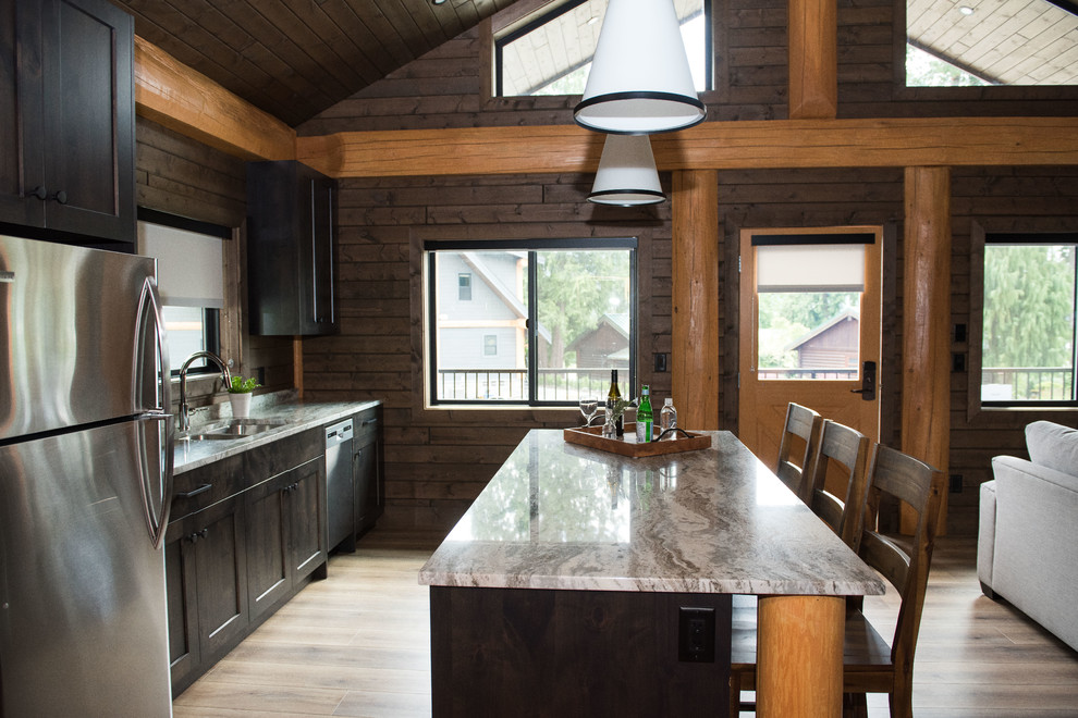 Inspiration för ett mellanstort rustikt grå linjärt grått kök med öppen planlösning, med en dubbel diskho, skåp i shakerstil, skåp i mörkt trä, granitbänkskiva, fönster som stänkskydd, rostfria vitvaror, laminatgolv, en köksö och brunt golv