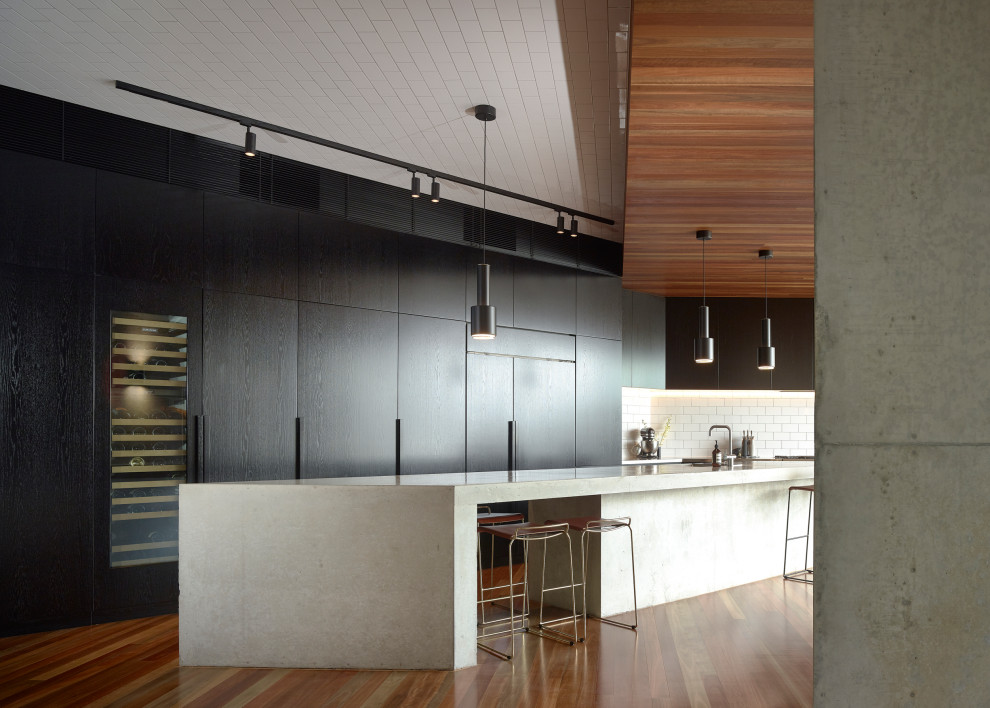 Inspiration for a contemporary galley medium tone wood floor and brown floor open concept kitchen remodel in Brisbane with flat-panel cabinets, black cabinets, white backsplash, subway tile backsplash, paneled appliances, an island and gray countertops