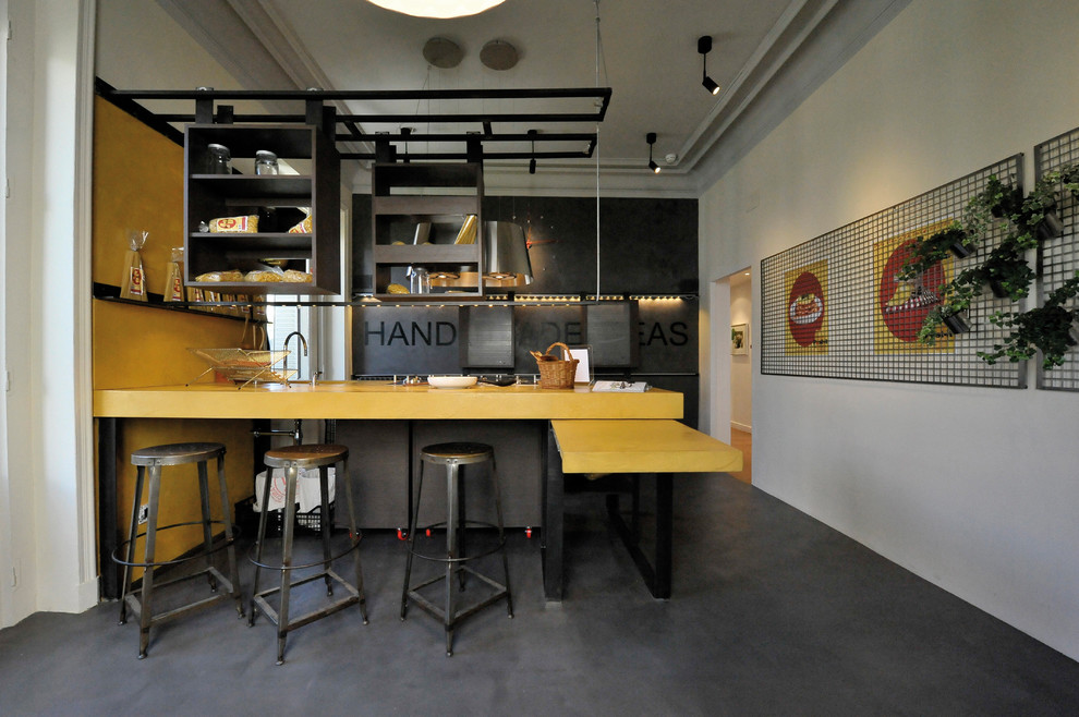 На фото: прямая кухня среднего размера в стиле лофт с обеденным столом, бетонным полом, открытыми фасадами, черными фасадами, столешницей из акрилового камня, желтым фартуком и полуостровом