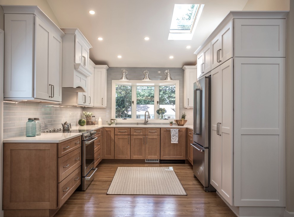 Example of a transitional u-shaped medium tone wood floor and brown floor kitchen design with shaker cabinets, medium tone wood cabinets, gray backsplash, no island and white countertops