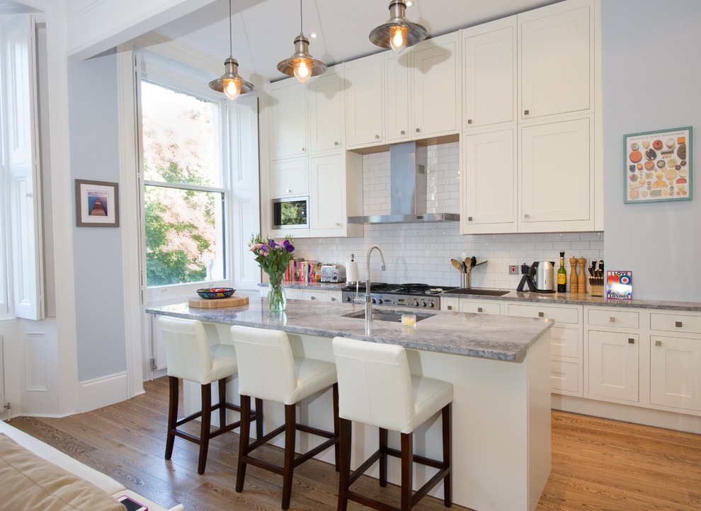 Mid-sized transitional single-wall medium tone wood floor and brown floor kitchen photo in London with an undermount sink, recessed-panel cabinets, beige cabinets, granite countertops, white backsplash, subway tile backsplash, stainless steel appliances, an island and gray countertops