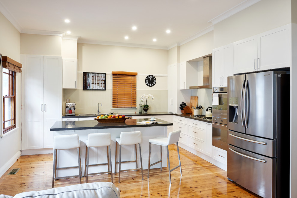 Immagine di una cucina design di medie dimensioni con lavello a doppia vasca, ante lisce, ante bianche, elettrodomestici in acciaio inossidabile e parquet chiaro