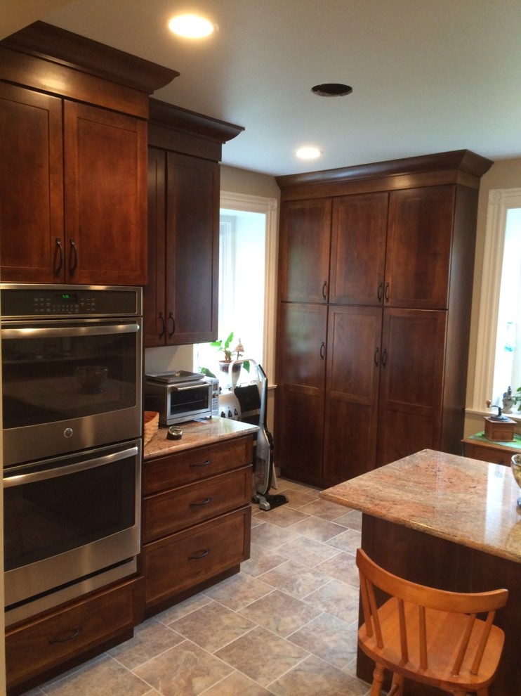 This is an example of a small country u-shaped kitchen pantry in Other with recessed-panel cabinets, dark wood cabinets, granite worktops, beige splashback, stainless steel appliances, an island, a submerged sink and porcelain flooring.