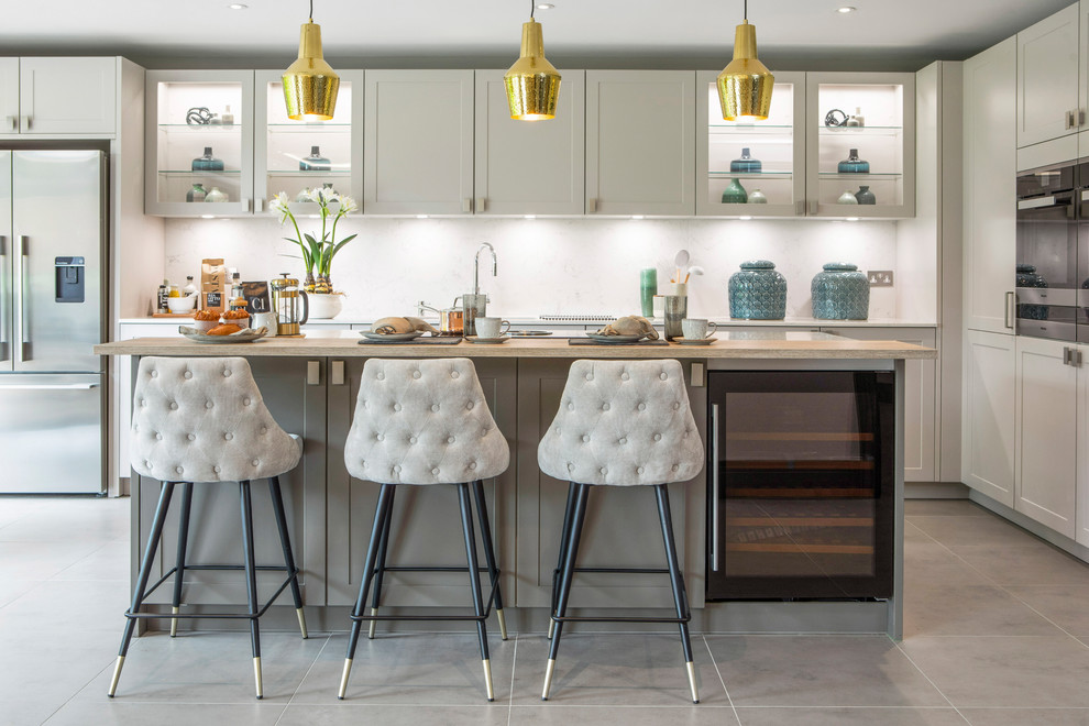 Moderne Küche in L-Form mit Kücheninsel, Schrankfronten im Shaker-Stil, grauen Schränken, Küchenrückwand in Weiß, Küchengeräten aus Edelstahl, grauem Boden und grauer Arbeitsplatte in London