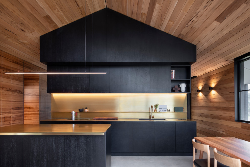 Cette image montre une cuisine américaine parallèle et encastrable design avec un évier encastré, un placard à porte plane, des portes de placard noires, une crédence métallisée, sol en béton ciré, une péninsule, un sol gris, un plafond voûté et un plafond en bois.
