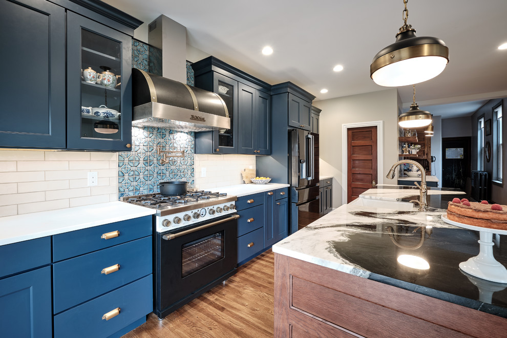 Inredning av ett eklektiskt stort flerfärgad flerfärgat kök, med en rustik diskho, luckor med infälld panel, blå skåp, bänkskiva i kvartsit, grått stänkskydd, stänkskydd i keramik, svarta vitvaror, mellanmörkt trägolv, en köksö och brunt golv