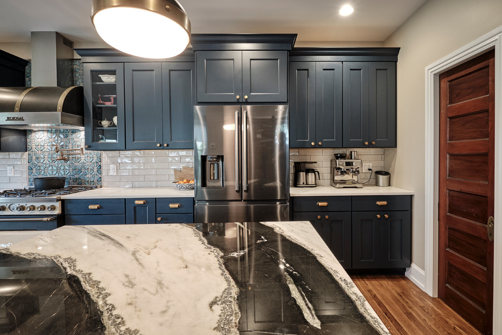 Large eclectic galley medium tone wood floor and brown floor open concept kitchen photo in Philadelphia with a farmhouse sink, recessed-panel cabinets, blue cabinets, quartzite countertops, gray backsplash, ceramic backsplash, black appliances, an island and multicolored countertops