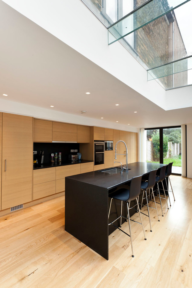 This is an example of a contemporary kitchen in London with a submerged sink, flat-panel cabinets, medium wood cabinets, light hardwood flooring and an island.