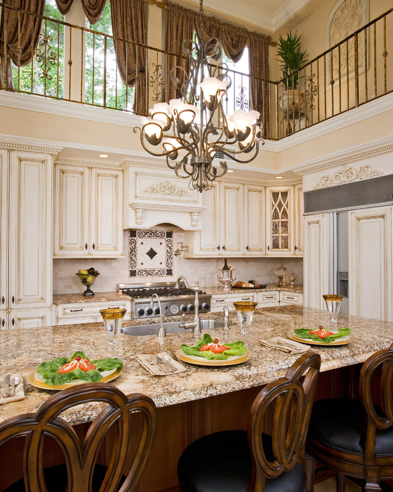 Large elegant l-shaped enclosed kitchen photo in Philadelphia with granite countertops, brown countertops, an undermount sink, raised-panel cabinets, beige cabinets, beige backsplash, travertine backsplash, paneled appliances and an island