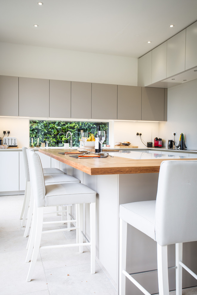 Photo of a medium sized contemporary u-shaped open plan kitchen in Hampshire with flat-panel cabinets, grey cabinets, stainless steel appliances, an island, composite countertops, grey splashback and glass sheet splashback.