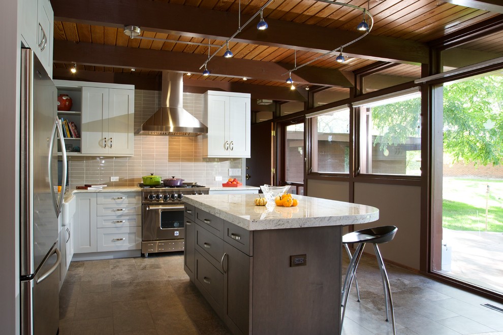 Example of a mid-sized trendy l-shaped travertine floor enclosed kitchen design in Chicago with a farmhouse sink, shaker cabinets, white cabinets, stainless steel appliances, an island, marble countertops, beige backsplash and porcelain backsplash