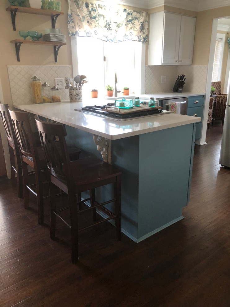 Modelo de cocinas en L marinera, de tamaño medio, con despensa, fregadero sobremueble, armarios estilo shaker, puertas de armario blancas, encimera de cuarcita, salpicadero blanco, salpicadero con mosaicos de azulejos, electrodomésticos de acero inoxidable, suelo laminado, península, suelo marrón y encimeras blancas