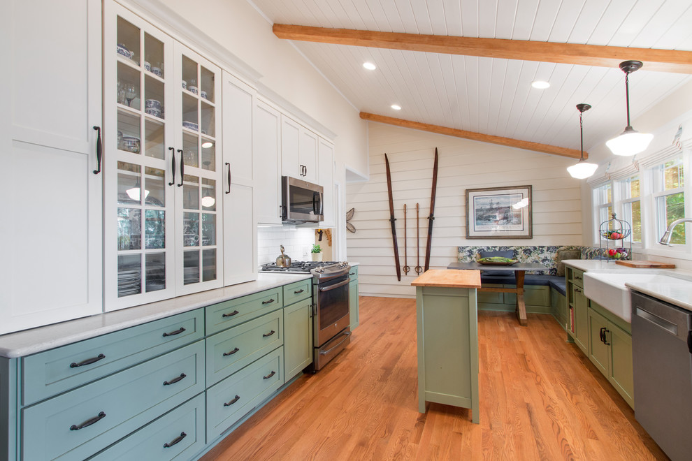 Mid-sized farmhouse galley light wood floor and beige floor eat-in kitchen photo in Milwaukee with a farmhouse sink, green cabinets, beige backsplash, subway tile backsplash, stainless steel appliances, an island, glass-front cabinets and quartz countertops