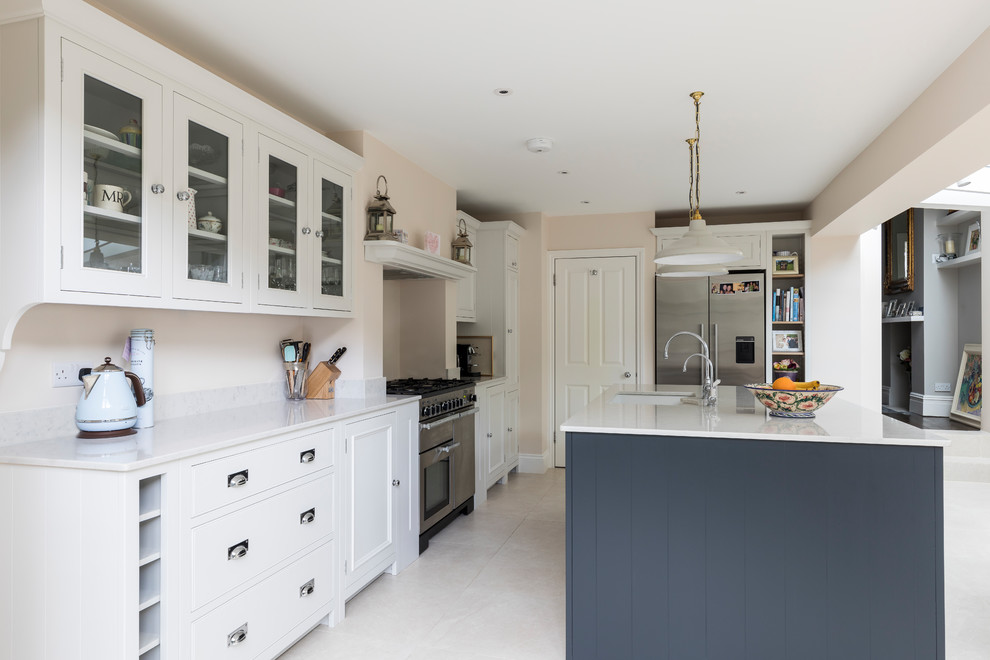 This is an example of a medium sized contemporary l-shaped kitchen/diner in London with a belfast sink, shaker cabinets, white cabinets, quartz worktops, stainless steel appliances, limestone flooring, an island and beige floors.