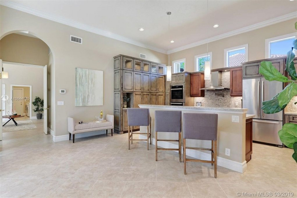 Example of a large transitional u-shaped travertine floor and beige floor eat-in kitchen design in Miami with an undermount sink, shaker cabinets, distressed cabinets, granite countertops, beige backsplash, stone tile backsplash, stainless steel appliances, an island and beige countertops