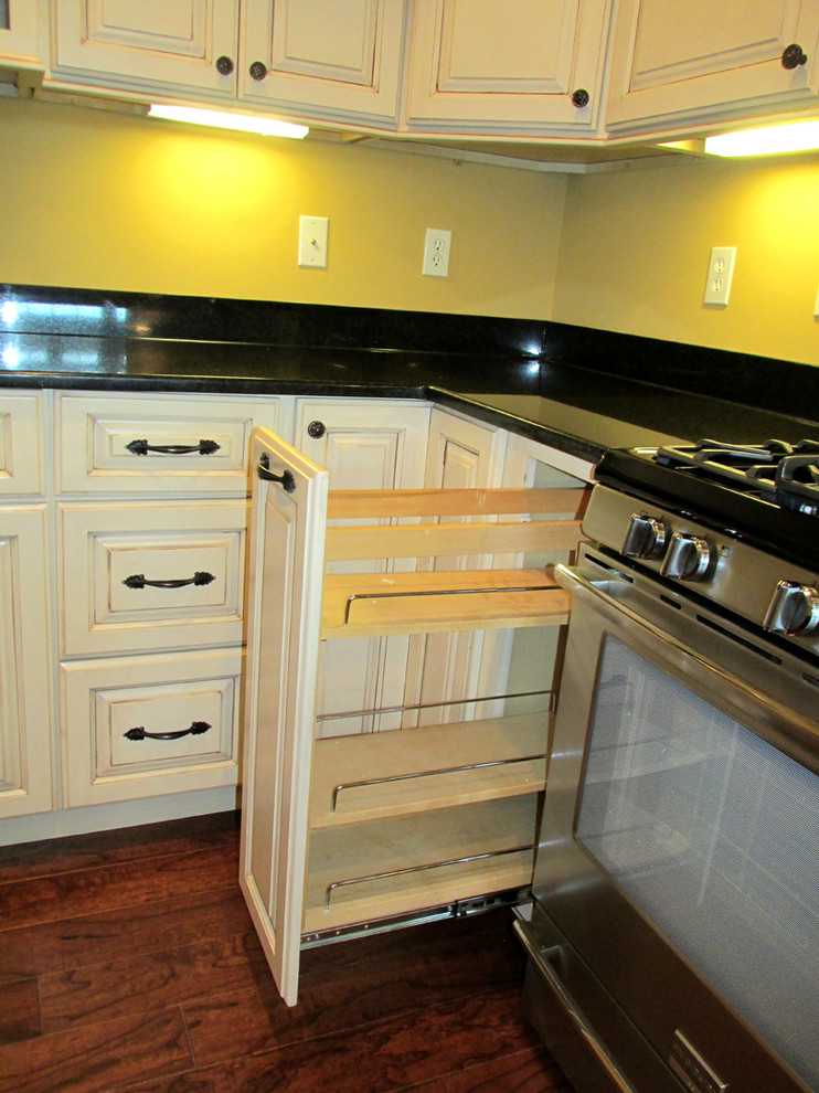 This is an example of a traditional l-shaped kitchen/diner in St Louis with a submerged sink, raised-panel cabinets, white cabinets, granite worktops, black splashback, stainless steel appliances and medium hardwood flooring.