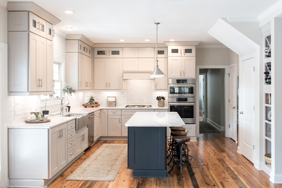 Idéer för ett mellanstort modernt vit l-kök, med en rustik diskho, skåp i shakerstil, vita skåp, marmorbänkskiva, vitt stänkskydd, stänkskydd i tunnelbanekakel, rostfria vitvaror, mellanmörkt trägolv, en köksö och brunt golv