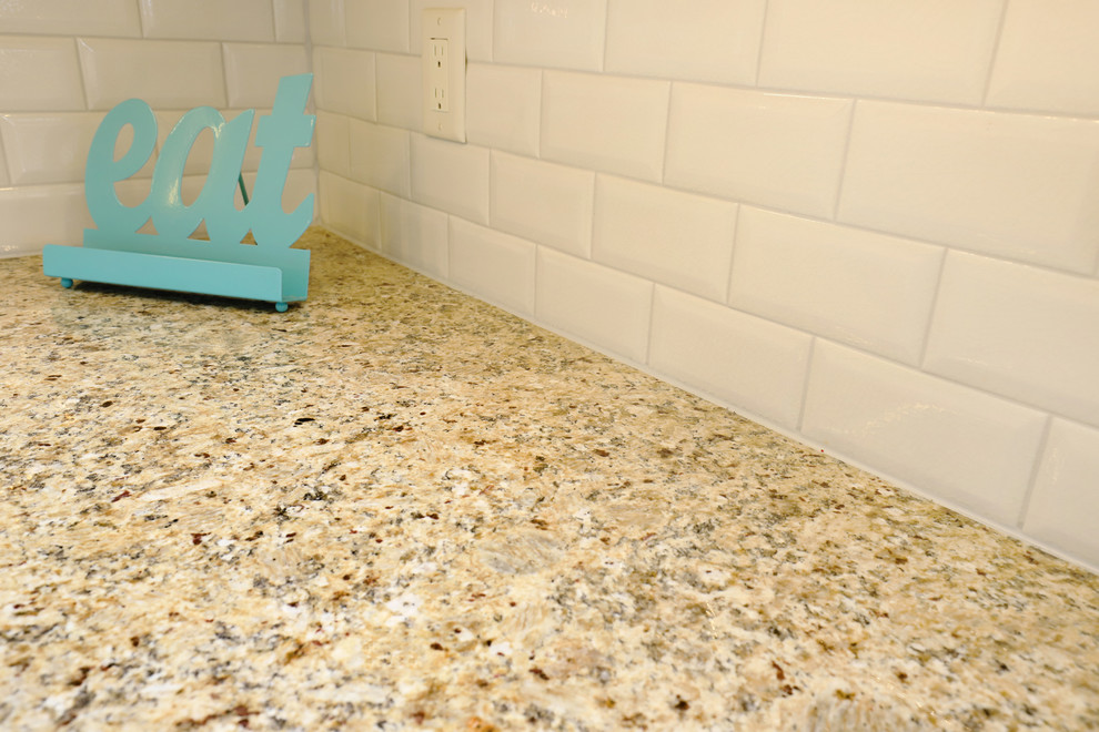 Klassisk inredning av ett mellanstort kök, med en undermonterad diskho, luckor med infälld panel, vita skåp, granitbänkskiva, vitt stänkskydd, stänkskydd i tunnelbanekakel, rostfria vitvaror, klinkergolv i keramik, en köksö och brunt golv