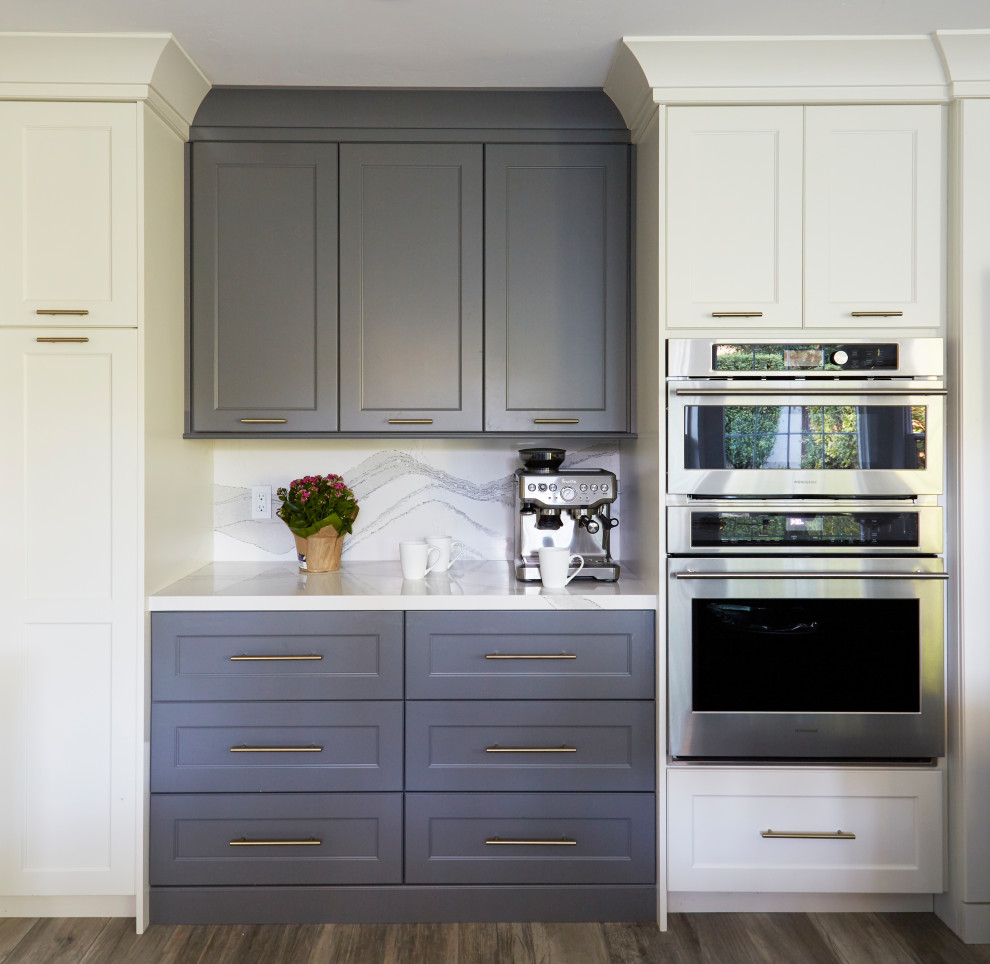 Foto på ett stort vintage vit kök, med en dubbel diskho, luckor med infälld panel, vita skåp, bänkskiva i kvarts, blått stänkskydd, stänkskydd i glaskakel, rostfria vitvaror, cementgolv, en köksö och brunt golv