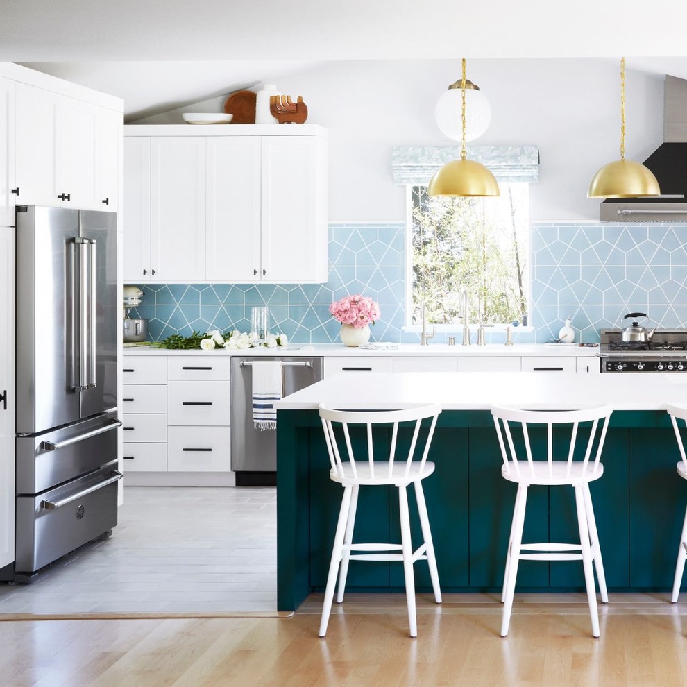 Cette photo montre une cuisine chic en L avec un plan de travail en quartz, une crédence bleue, un électroménager en acier inoxydable, îlot, un plan de travail blanc, un placard à porte shaker, des portes de placard blanches et un sol gris.