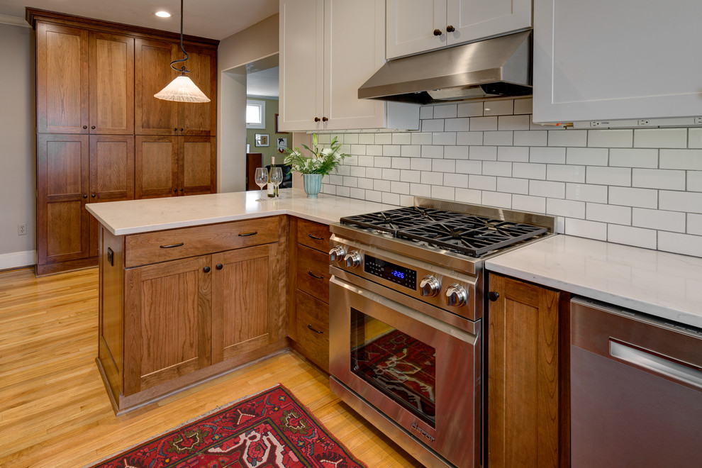 Example of a small classic u-shaped medium tone wood floor enclosed kitchen design in Columbus with a single-bowl sink, shaker cabinets, medium tone wood cabinets, granite countertops, white backsplash, subway tile backsplash, stainless steel appliances, a peninsula and white countertops
