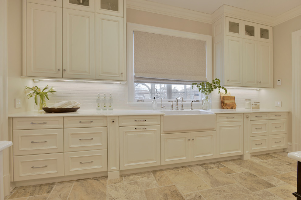Huge elegant u-shaped travertine floor and multicolored floor eat-in kitchen photo in New York with a farmhouse sink, raised-panel cabinets, white cabinets, marble countertops, white backsplash, subway tile backsplash, paneled appliances and an island