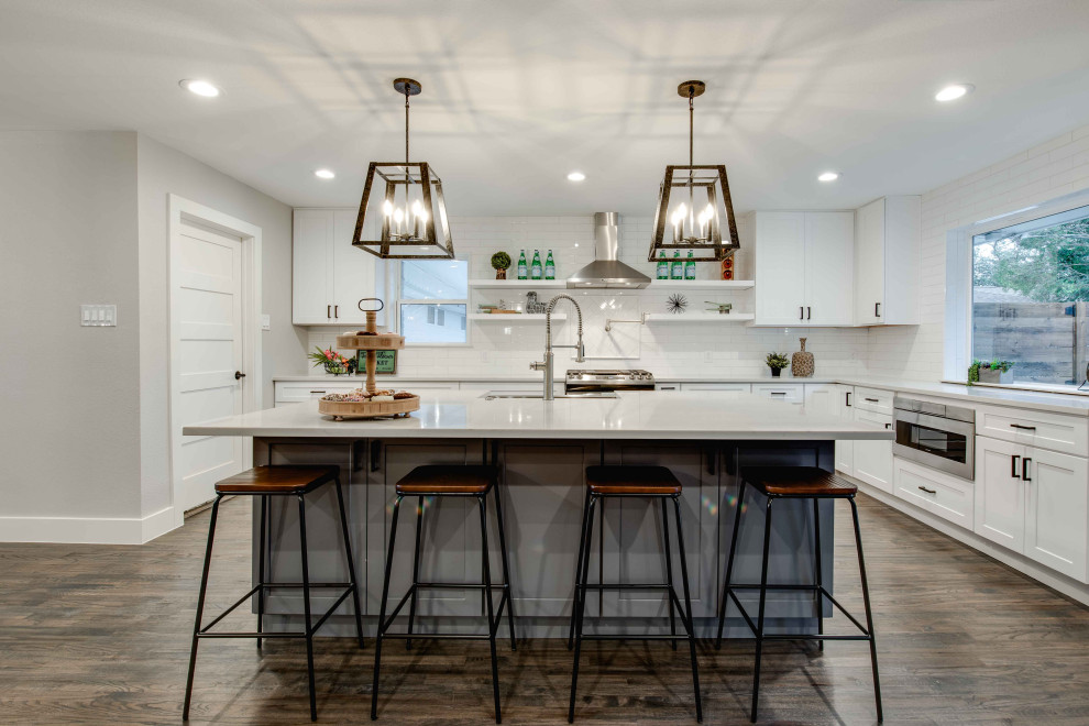Photo of a traditional l-shaped kitchen in Dallas with a belfast sink, shaker cabinets, white cabinets, white splashback, stainless steel appliances, dark hardwood flooring, an island, brown floors and white worktops.