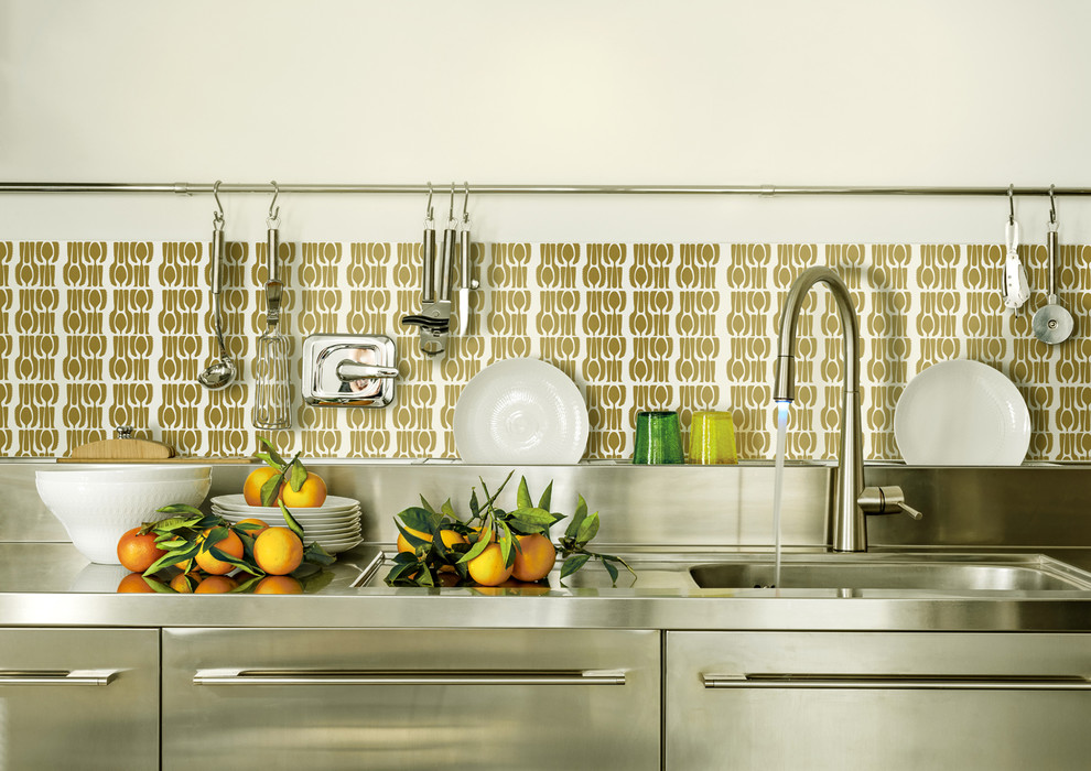 Bild på ett industriellt kök, med en integrerad diskho, skåp i rostfritt stål, bänkskiva i rostfritt stål, stänkskydd med metallisk yta och rostfria vitvaror