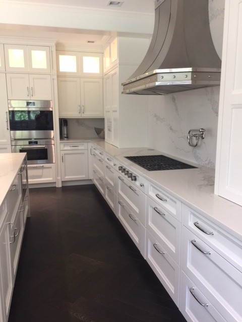 Foto på ett stort vintage vit kök, med en rustik diskho, luckor med infälld panel, vita skåp, vitt stänkskydd, integrerade vitvaror, vinylgolv, en köksö, svart golv och bänkskiva i kvarts