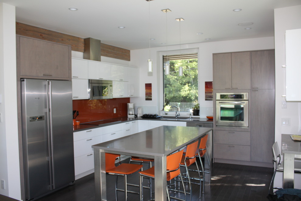 This is an example of a medium sized contemporary l-shaped open plan kitchen in Vancouver with a submerged sink, flat-panel cabinets, grey cabinets, orange splashback, glass sheet splashback, stainless steel appliances, dark hardwood flooring and an island.