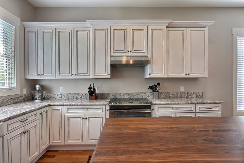 Lantlig inredning av ett stort kök, med en rustik diskho, luckor med upphöjd panel, blå skåp, träbänkskiva, rostfria vitvaror, mellanmörkt trägolv, en köksö och vitt stänkskydd